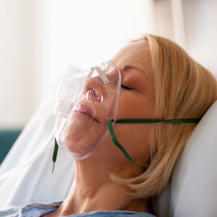 A woman in an oxygen mask lying in a hospital bed.